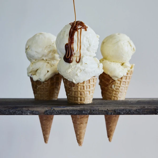 Three ice cream cones with vanilla ice cream and chocolate drizzle on top.