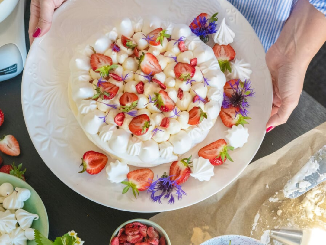 Pavlova med frasig marängbas, överdragen med jordgubbscurd och vispad grädde, serverad som midsommardessert.